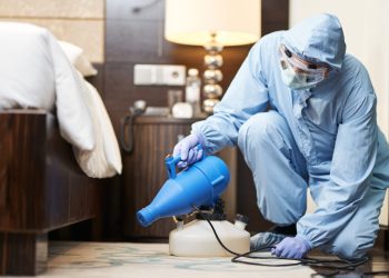 Man in biohazard suit and gloves disinfecting bedroom in hotel. Coronavirus and quarantine concept